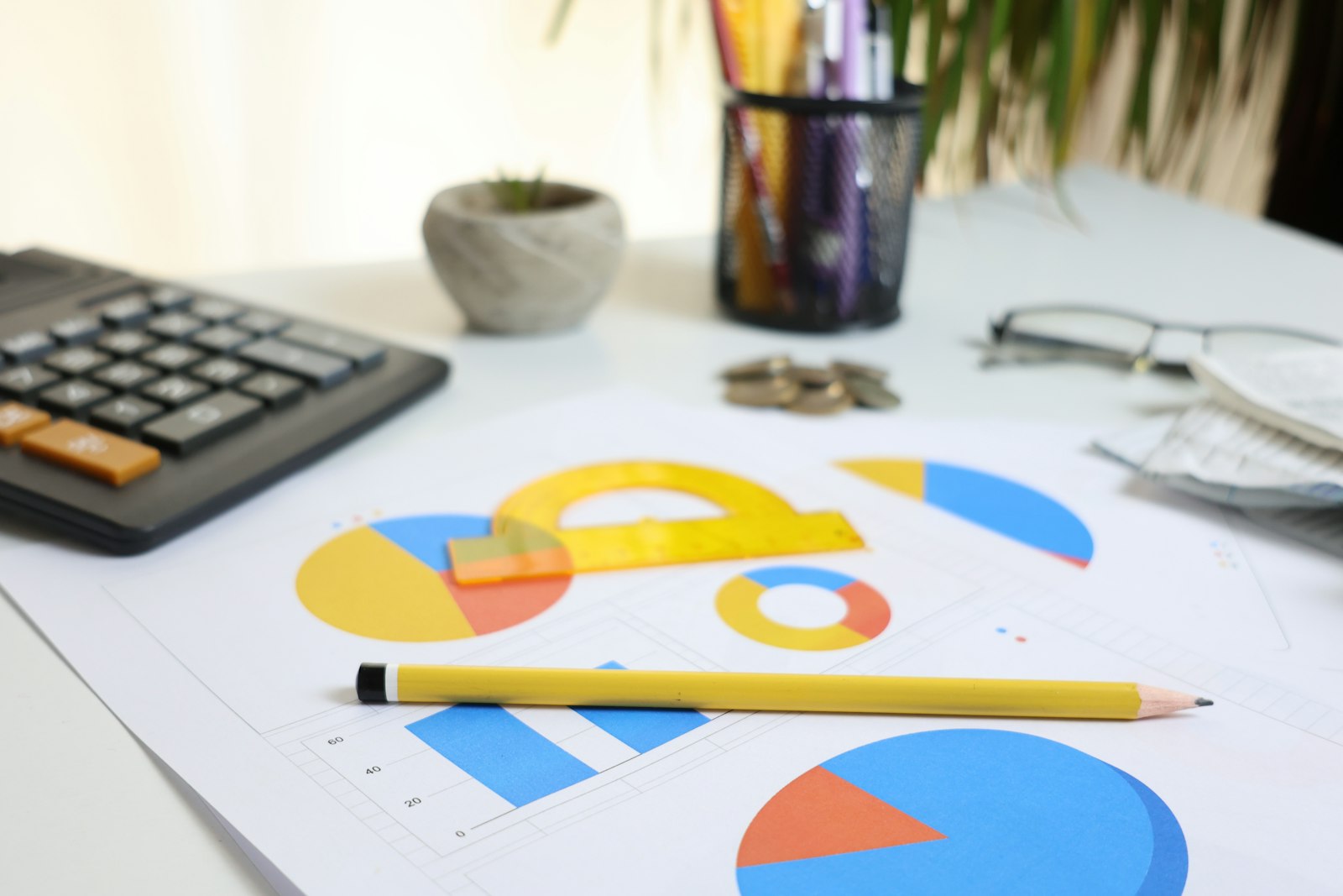Graphiques et camemberts colorés imprimés sur une feuille, avec crayon, calculatrice et lunettes, sur un bureau.