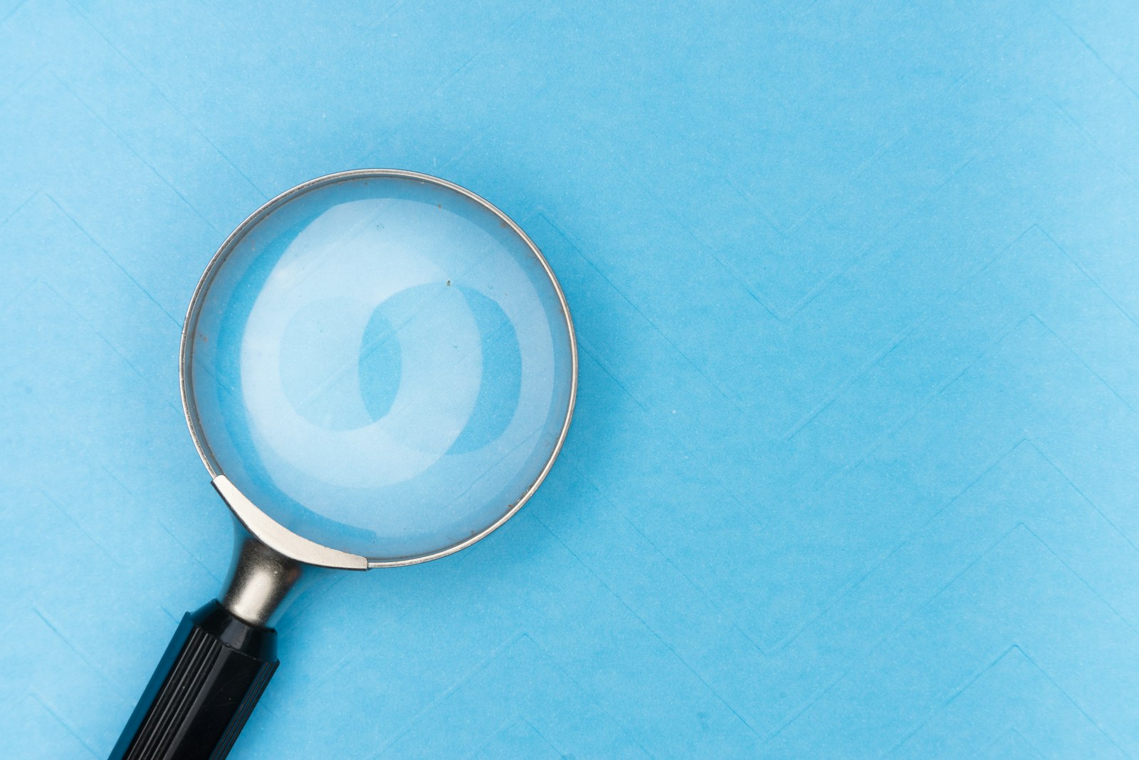 Loupe posée sur un fond bleu, illustrant l’examen et la vérification d’une information.