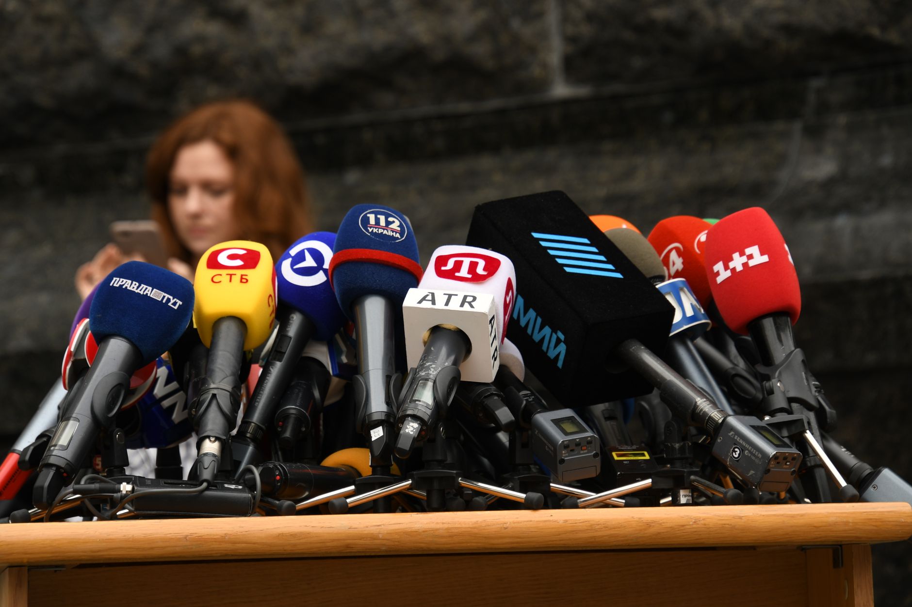 Mur de microphones de télévision devant un pupitre vide, avant une prise de parole publique.